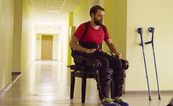 Disable man in the robotic exoskeleton sitting on the bench and taking off exoskeleton