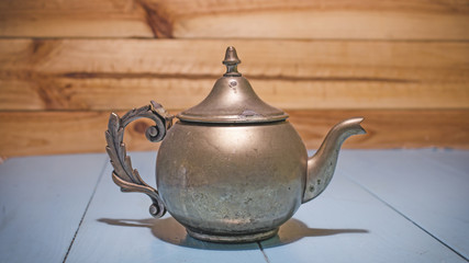 Beautiful vintage copper teapot kettle with tarnished metal, sitting in blue wooden surface. Old teapot with abrasions.