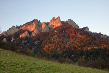 Three Crowns massive in Pieniny Mountains, Poland, view from valley in Sromowce Niżne, evening sunlight, blue sky, autumn season, colorful trees cover hill.