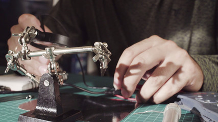 Crane. Close up. Repairing of wire for electronic devices. Male hands measuring voltage in the wire using magnifying glass
