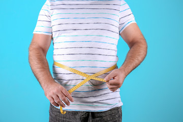 Fat man with measuring tape on color background, closeup. Weight loss