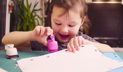 Scrapbooking. Little girl doing a postcard. She is cutting flowers from a paper. Children's creativity, handicraft