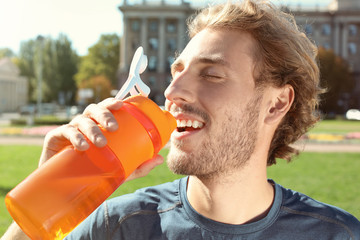 Young man drinking clean water from bottle on city street
