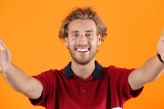 Handsome young man laughing and taking selfie on color background