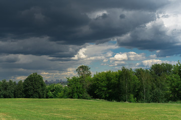 Fototapeta premium Storm clouds over the trees and green grass field in Kolomenskoye Park in summer.