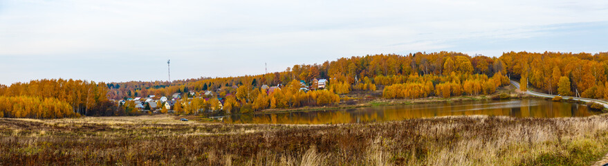 The village on the background of the autumn forest on the lake. Autumn in Russia