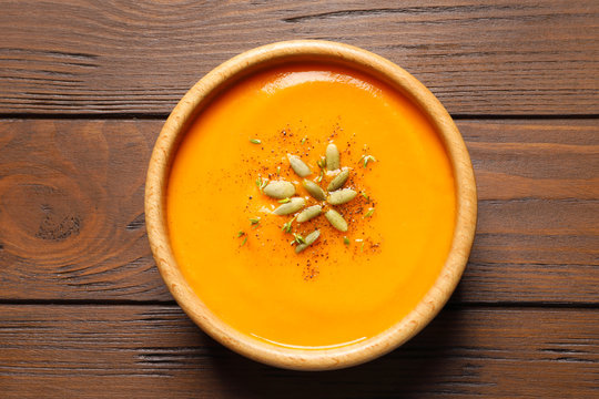 Bowl with tasty pumpkin soup on wooden table, top view