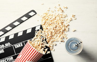 Tasty popcorn, drink and clapperboard on wooden background, top view. Cinema snack