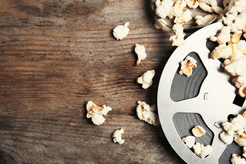 Obraz na płótnie Canvas Tasty popcorn and film reel on wooden background, top view with space for text