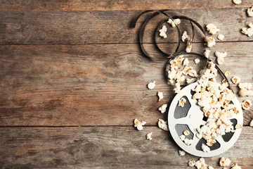 Poster Tasty popcorn and film reel on wooden background, top view with space for text © New Africa