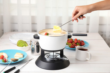Woman dipping pineapple into pot with white chocolate fondue on table