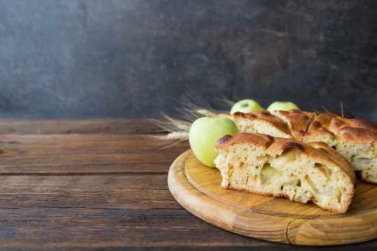 Round home-made apple pie, cobbler, brown Betty, Apple Charlotte on wooden background with apples and spikelets.