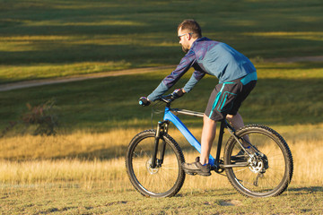 Fototapeta premium A cyclist rides the hills, Beautiful portrait of a guy on a blue bicycle