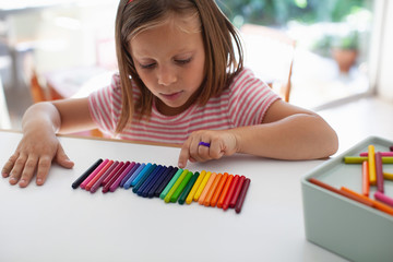 A child lines up colorful crayons in a row. 