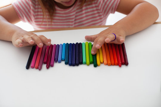 A child lines up colorful crayons in a row. 