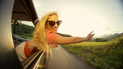 CLOSE UP: Carefree blonde girl waving her hands through the air while driving.