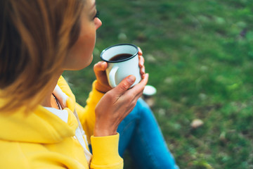 Happy girl holding in hands cup of hot tea on green grass in outdoors nature park, beautiful woman hipster enjoy drinking cup of coffee closeup, lifestyle relax recreation meditation concept