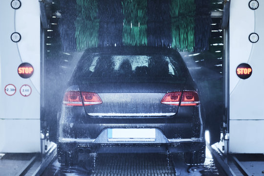 Back View Of A Carwash Cleaning A Car With Rotating Brushes.