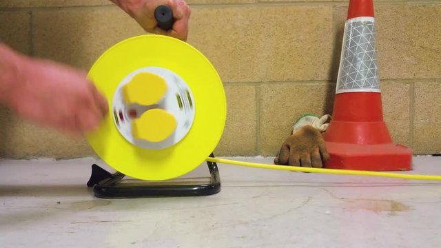 Yellow extension lead drum being reeled in by an engineer along a plant room floor