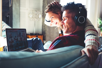 Happy couple in love at home. Man and woman sitting on the couch and watching TV series on laptop and listening music. Bright loft apartment