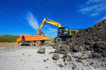 Clay mining. Yellow excavator loads raw materials in the truck on blue sky background