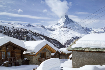 Village Eggen in winter with deep snow covered roofs under the famous Alps landmark Matterhorn,...