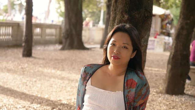 relaxed attractive young asian woman in the park looking at camera