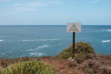 fall hazard (spanish: Peligro De Caidas) warning sign with ocean landscape background   -