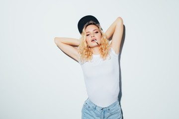 Portrait of young blonde woman with cigarette dressed in white t-shirt wearing cap standing isolated over white background