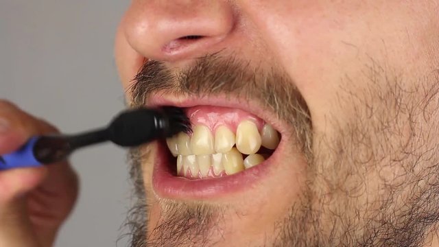 side view of man mouth with beard and mustache thoroughly brushes his teeth with black toothbrush without toothpaste, movements from top to bottom and from bottom to top, gum massage, closeup