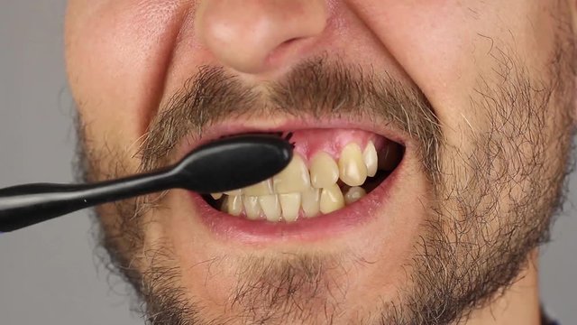 man with beard and mustache thoroughly brushes his teeth with black toothbrush without toothpaste, proper movements from top to bottom and from bottom to top, gum massage, front view, closeup