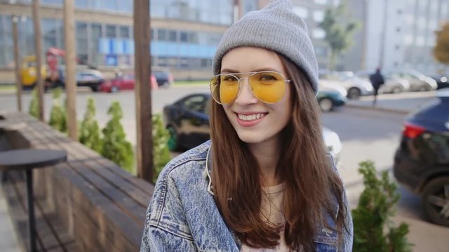 Portrait of smiling hipster girl wearing sunglasses and hat, urban background