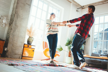 Couple in love at home. Spending happy time and dancing in the big spacious room, laughting and hugging. Bright loft apartment