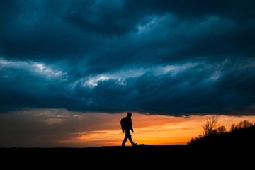 Man silhouette walking against dramatic clouds background