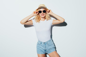 Naklejka premium Portrait of a pretty beautiful blonde wearing beach hat, sunglasses and summer clothes isolated on the white background