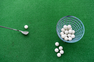 Golf club and balls on a synthetic grass mat at a practice range.