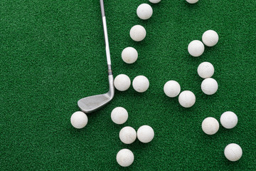 Golf club and balls on a synthetic grass mat at a practice range.