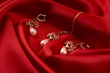Beautiful precious women's jewelry, close-up. Pearl Golden Necklace and Earrings on red silk background with copy space