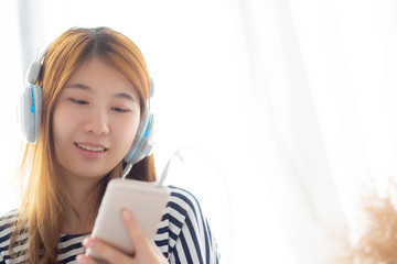 Naklejka premium Beautiful asian young woman enjoy listen music with headphone and holding smart mobile phone while sitting in bedroom, relax girl with earphone, leisure and technology concept.