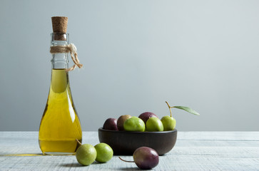 glass bottle of olive oil and wooden breakfast  bowl with raw turkish olive seeds and leaf on white...