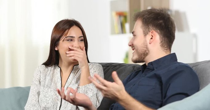 Embarrassed girl talking with a man during a date hiding smile with her hand at home