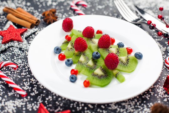 Kiwi christmas tree with raspberry, blueberry and cowberry on table with decoration