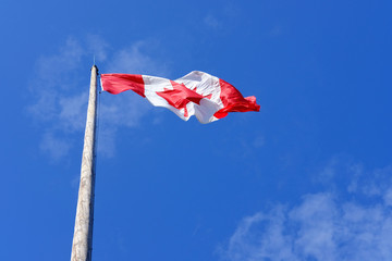 Canadian flag in blue sky background, fluttering in wind, sunny day