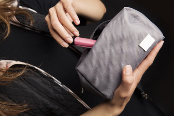 Mujer jóven sacando lápiz labial de bolsa de cosméticos