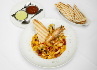 Paella valenciana española arroz amarillo en un plato blanco acompañada por pan