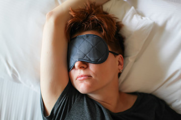 Adult beautiful caucasian woman sleeping in white bed with gray eye mask