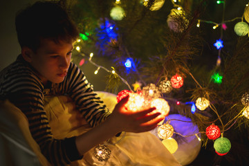 cute young boy in pajamas holds  lights garland in the evening at home. Winter holidays, New year and Christmas celebration concept. soft focus