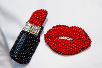 Two brooches woven from beads in the form of lipstick and red lips.