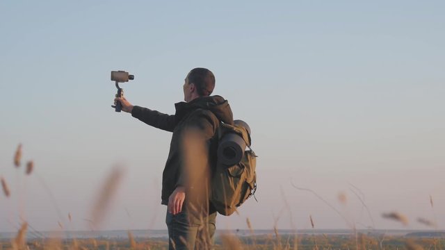 The man tourist hold stabilizer camera with a phone on the sunset background. He takes a selfie and takes a video.