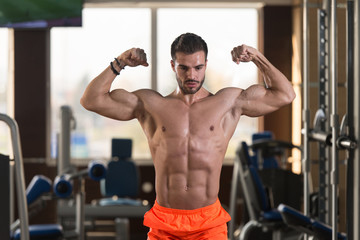 Fototapeta na wymiar Handsome Muscular Man Flexing Muscles In Gym